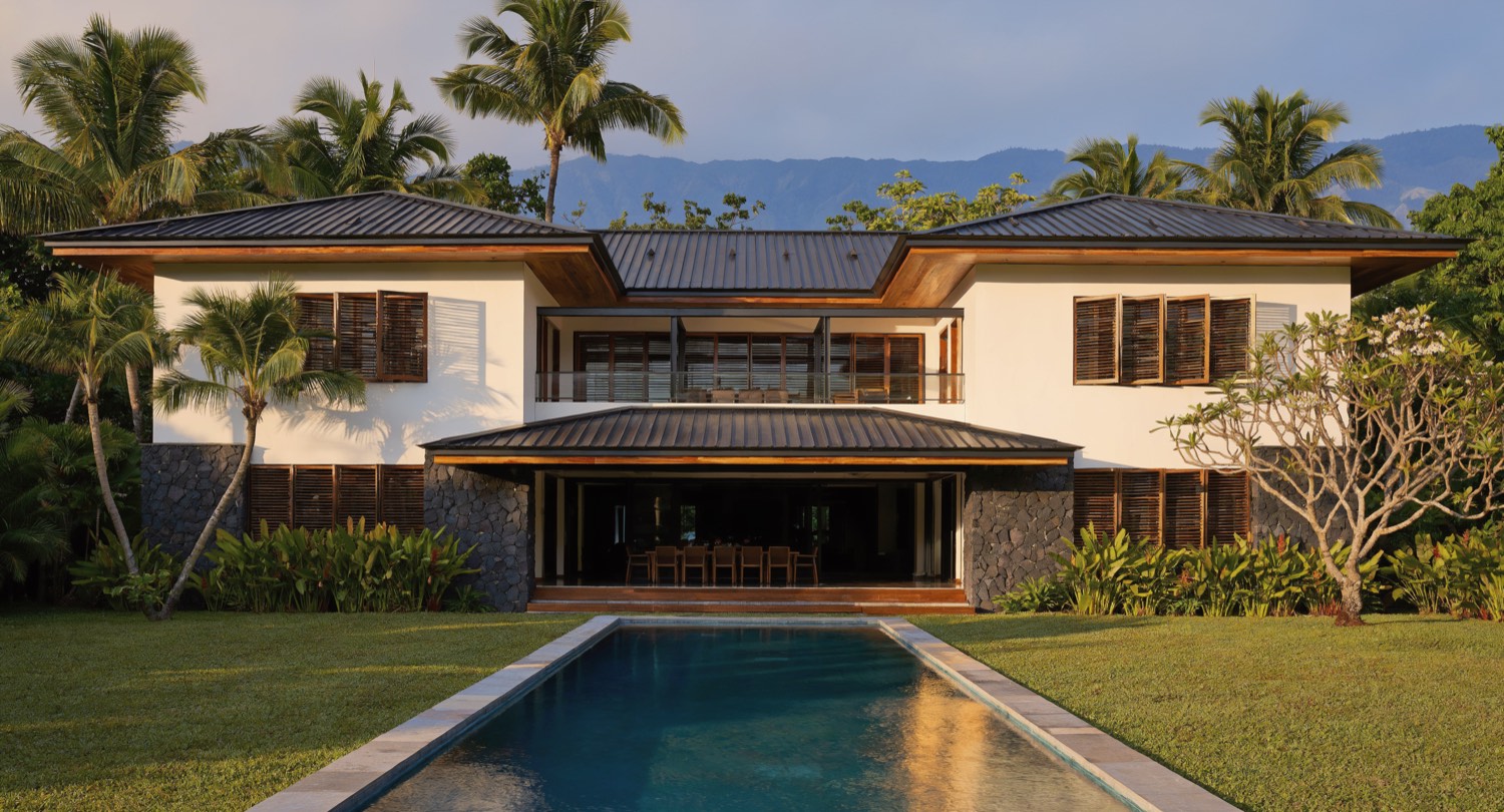 Artist's impression of the garden side of the Pavilion: a deep covered lanai
            under a wide-eaved roof, glass walls slid open to it, and a long pool in the
            lawn beyond.